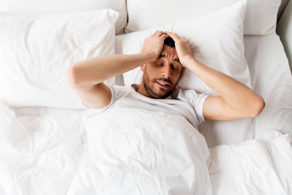 man lying in bed at home suffering from headache or hangover