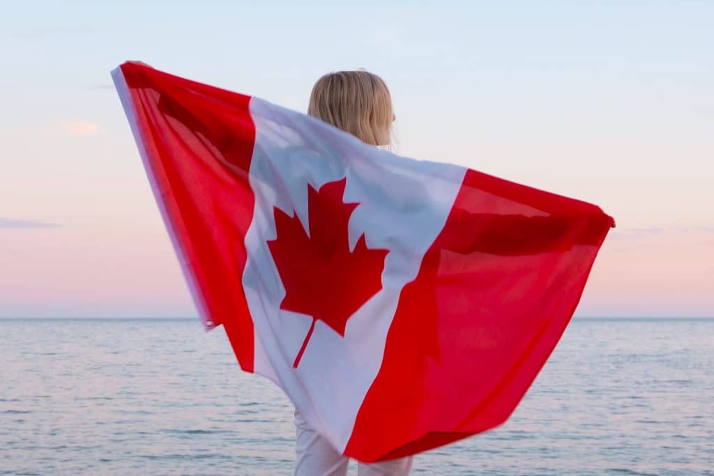 Back view woman waving national canada flag outdoors ocean sea sunset at summer 